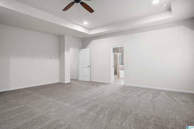 unfurnished room with ceiling fan, light colored carpet, and a tray ceiling