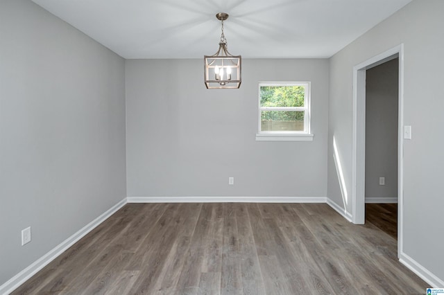 spare room with a notable chandelier and dark wood-type flooring