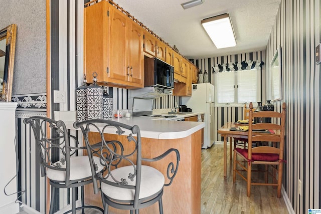 kitchen featuring white fridge, kitchen peninsula, light hardwood / wood-style flooring, a textured ceiling, and a kitchen breakfast bar