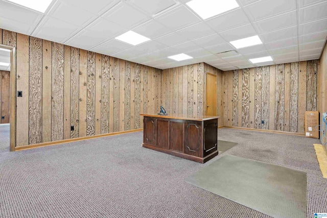 unfurnished office featuring wood walls, a paneled ceiling, and light colored carpet
