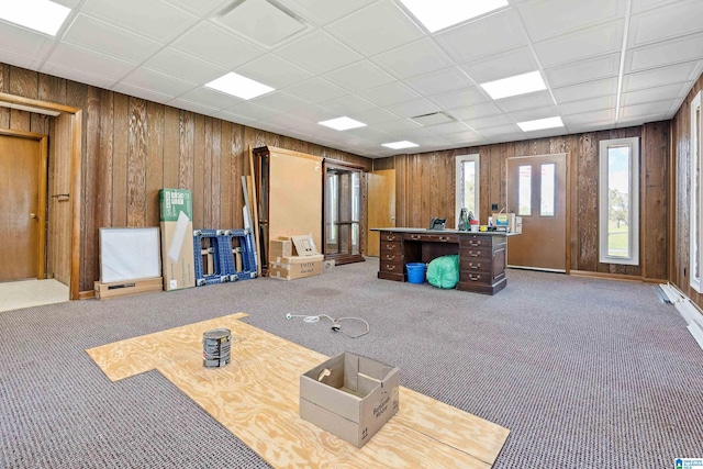 interior space featuring wooden walls, a drop ceiling, and dark colored carpet