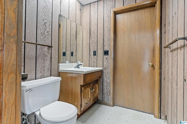 bathroom featuring tile floors, toilet, wood walls, and vanity with extensive cabinet space
