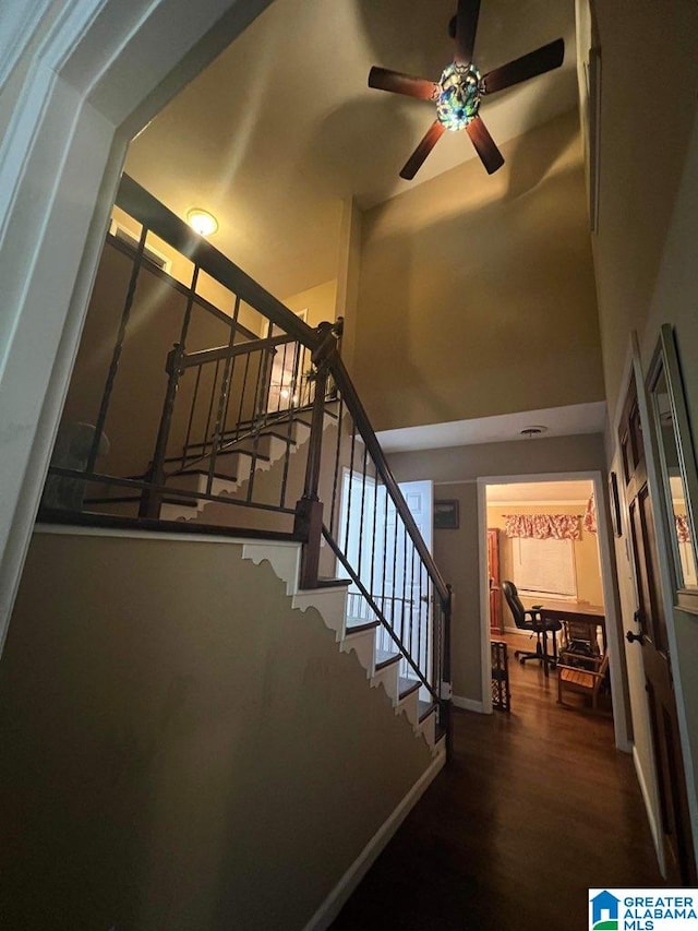 staircase featuring ceiling fan, dark wood-type flooring, and a towering ceiling