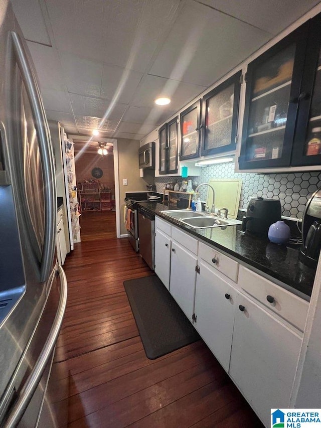 kitchen featuring dark hardwood / wood-style flooring, appliances with stainless steel finishes, white cabinets, dark stone countertops, and sink