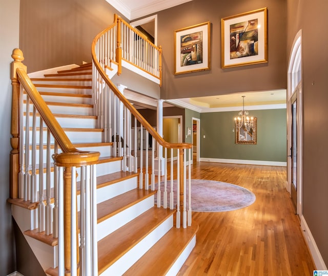 staircase featuring crown molding, a notable chandelier, and wood-type flooring