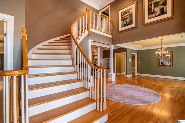 stairs with ornamental molding, decorative columns, hardwood / wood-style flooring, and an inviting chandelier