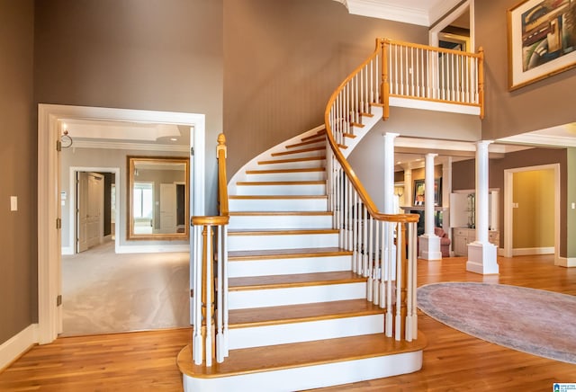 stairway with a towering ceiling, crown molding, hardwood / wood-style flooring, and decorative columns