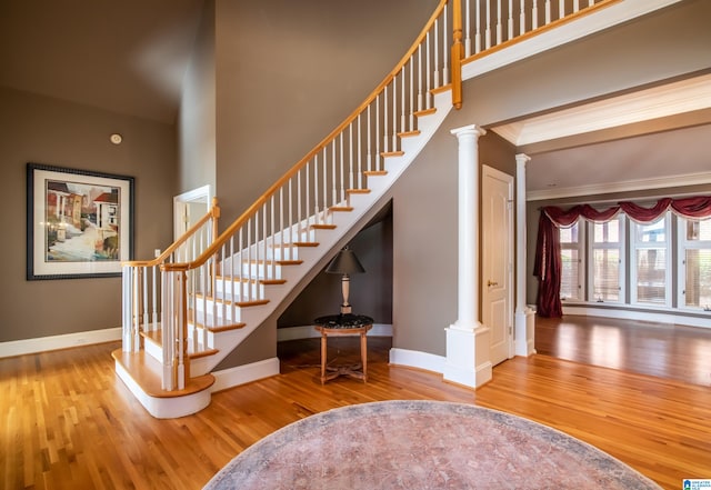 stairs featuring a towering ceiling, ornate columns, wood-type flooring, and ornamental molding