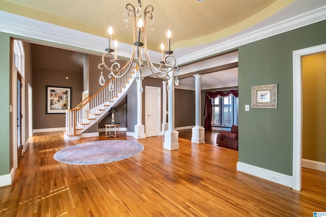 unfurnished dining area featuring ornamental molding, an inviting chandelier, hardwood / wood-style floors, and decorative columns