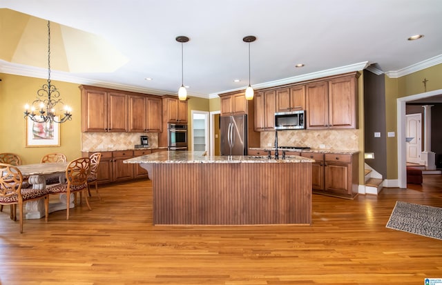 kitchen featuring light hardwood / wood-style flooring, stainless steel appliances, decorative light fixtures, and a kitchen island with sink