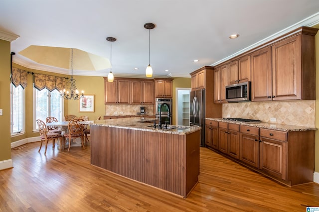 kitchen with a kitchen island with sink, appliances with stainless steel finishes, decorative light fixtures, and light wood-type flooring