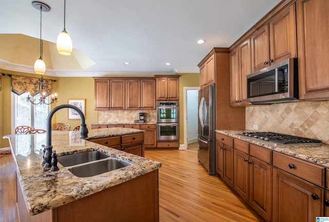 kitchen with appliances with stainless steel finishes, an island with sink, light hardwood / wood-style floors, pendant lighting, and ornamental molding