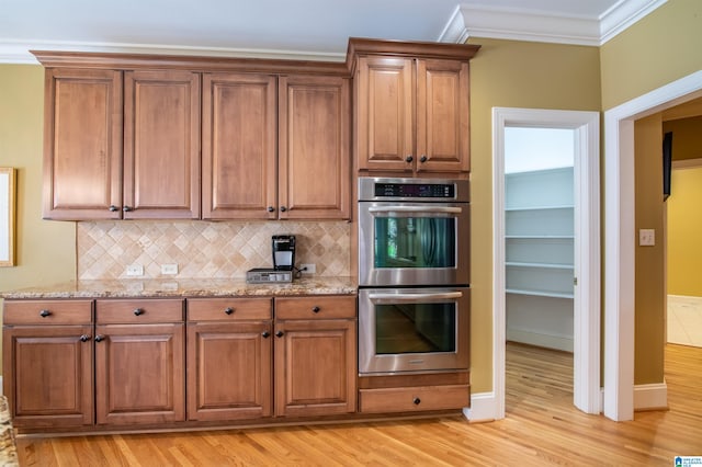 kitchen featuring stainless steel double oven, decorative backsplash, ornamental molding, light stone countertops, and light wood-type flooring