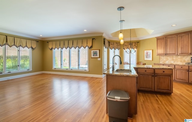 kitchen featuring light hardwood / wood-style flooring, ornamental molding, hanging light fixtures, and a center island with sink