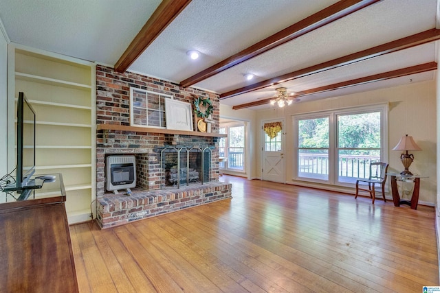 living room with beamed ceiling, light hardwood / wood-style floors, a brick fireplace, and a textured ceiling