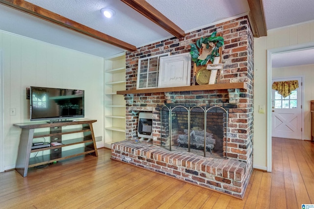 living room with beamed ceiling, a brick fireplace, light wood-type flooring, and a textured ceiling