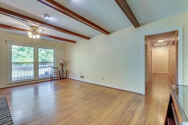 empty room with light hardwood / wood-style floors, ceiling fan, beamed ceiling, and a textured ceiling