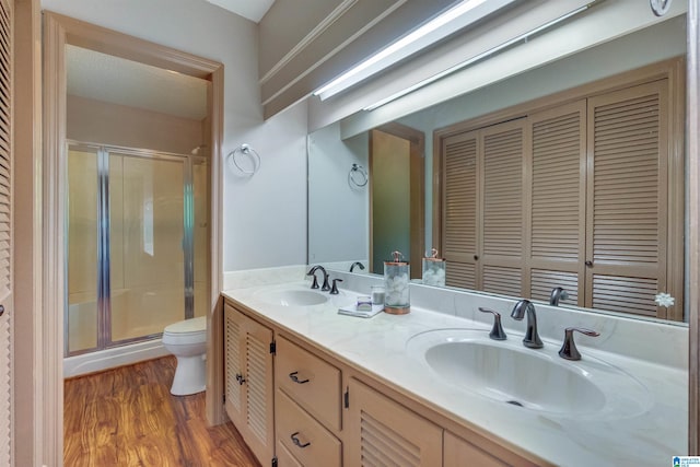 bathroom featuring a shower with door, large vanity, double sink, hardwood / wood-style flooring, and toilet