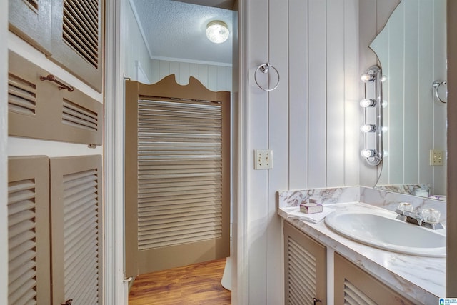 bathroom featuring wood-type flooring, a textured ceiling, vanity, and crown molding