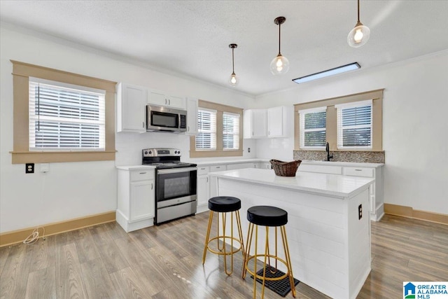 kitchen with pendant lighting, white cabinets, appliances with stainless steel finishes, and light hardwood / wood-style flooring