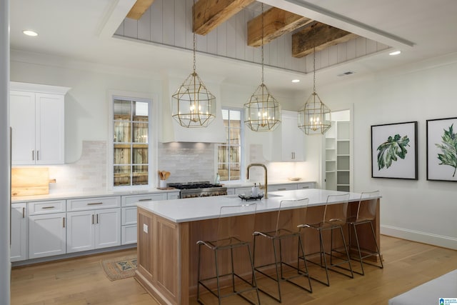 kitchen with light hardwood / wood-style flooring, stainless steel range oven, pendant lighting, a kitchen island with sink, and white cabinets