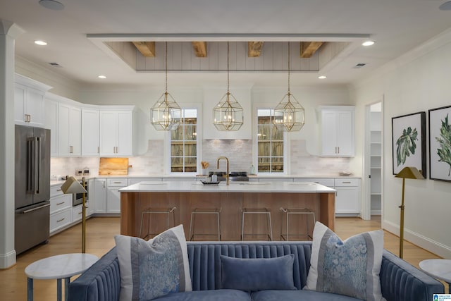 kitchen with high end fridge, backsplash, white cabinets, and a kitchen island with sink