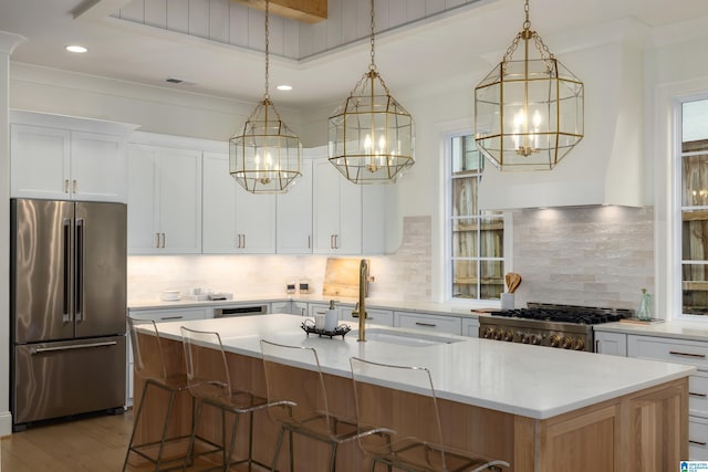 kitchen featuring white cabinets, appliances with stainless steel finishes, a center island with sink, and hanging light fixtures