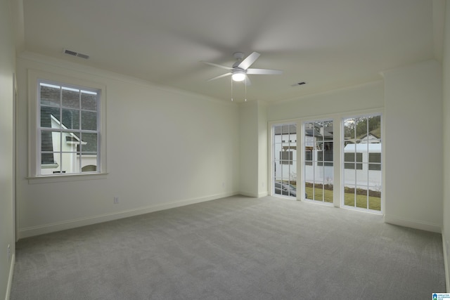 carpeted empty room featuring a wealth of natural light, ornamental molding, and ceiling fan