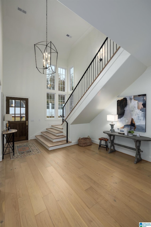 foyer with a towering ceiling, light hardwood / wood-style floors, plenty of natural light, and a notable chandelier