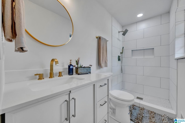 bathroom featuring toilet, tiled shower, and vanity