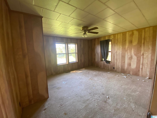 carpeted empty room with wooden walls and ceiling fan