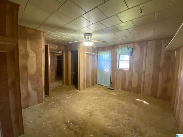 basement featuring ceiling fan and wooden walls