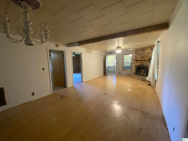 unfurnished living room featuring an inviting chandelier, light wood-type flooring, and a stone fireplace