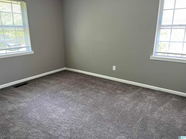 unfurnished room featuring plenty of natural light and dark carpet