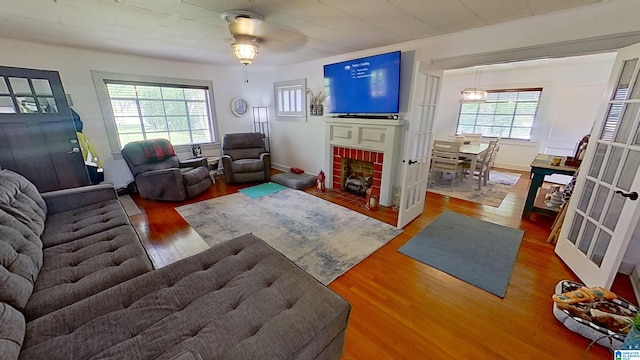 living room featuring plenty of natural light, dark wood-type flooring, a brick fireplace, and ceiling fan