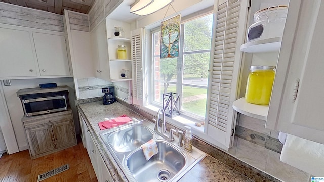 kitchen featuring white cabinets, sink, light stone countertops, and stainless steel microwave