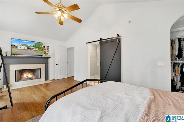 bedroom featuring high vaulted ceiling, ceiling fan, a barn door, light wood-type flooring, and a closet