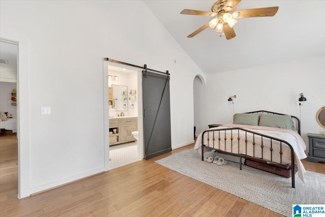 bedroom featuring high vaulted ceiling, ensuite bathroom, light hardwood / wood-style flooring, ceiling fan, and a barn door