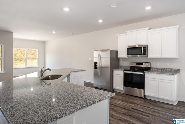 kitchen with sink, white cabinetry, dark stone counters, stainless steel appliances, and a center island with sink