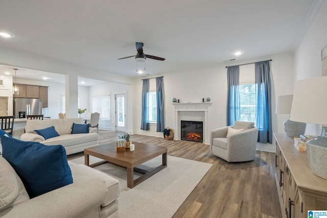 living room featuring ornamental molding, a healthy amount of sunlight, dark wood-type flooring, and ceiling fan