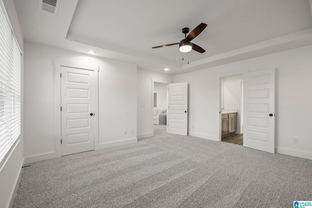 unfurnished bedroom with a closet, ceiling fan, light carpet, connected bathroom, and a raised ceiling