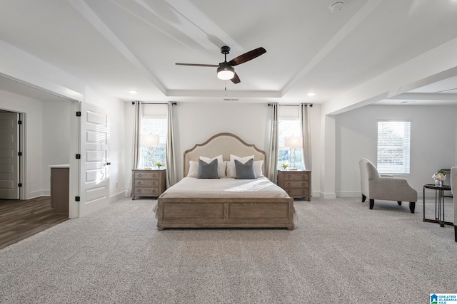 carpeted bedroom featuring ceiling fan and a raised ceiling