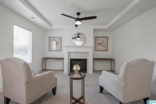 carpeted living room featuring a fireplace, a raised ceiling, and ceiling fan