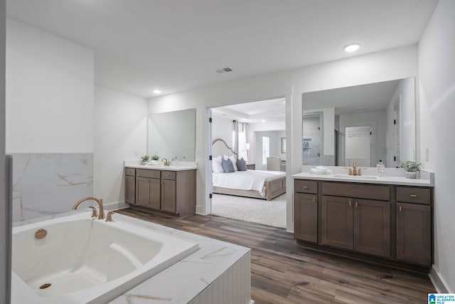 bathroom with hardwood / wood-style floors, a bath to relax in, and dual bowl vanity