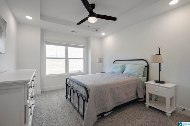 carpeted bedroom with ceiling fan and a raised ceiling