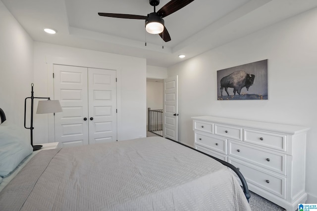 carpeted bedroom with a closet, ceiling fan, and a raised ceiling