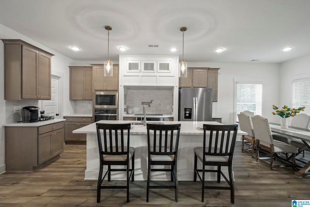 kitchen featuring appliances with stainless steel finishes, tasteful backsplash, a center island with sink, and dark wood-type flooring