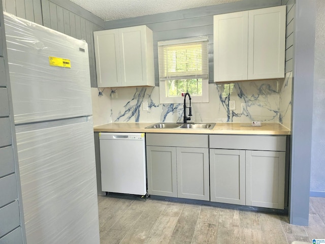 kitchen with backsplash, white appliances, white cabinets, sink, and light wood-type flooring