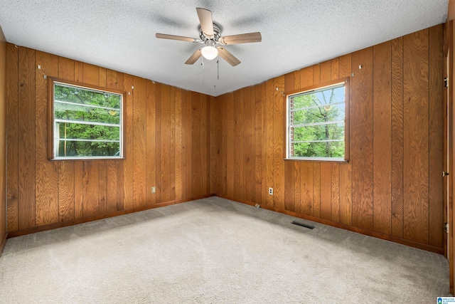 empty room with light colored carpet, plenty of natural light, wood walls, and ceiling fan