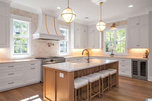 kitchen with backsplash, wine cooler, an island with sink, high end stainless steel range, and sink